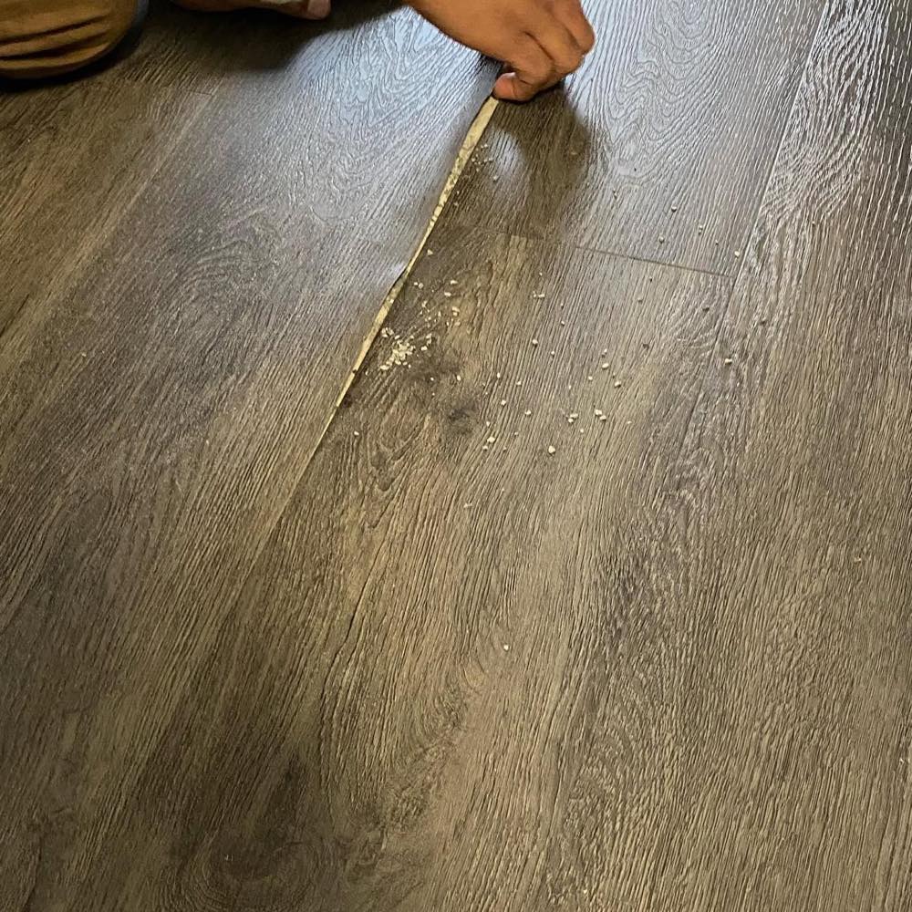 Before repair: a lifted, separated seam in a wide-plank floor with debris in the open joint